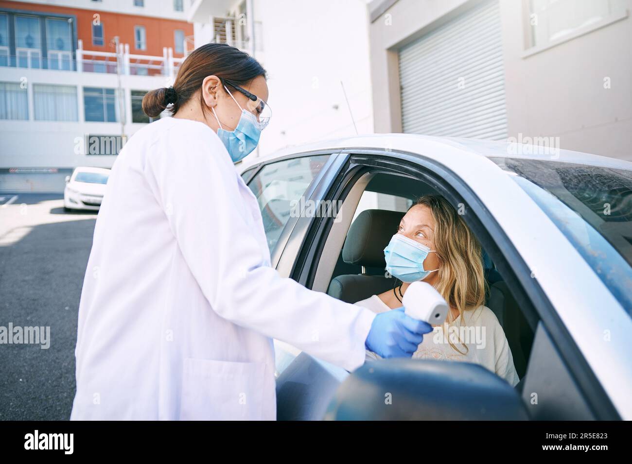 Achten Sie darauf, dass die Temperatur auf der Markierung liegt. Eine maskierte junge Frau, die sich von einem Arzt die Temperatur messen lässt, während sie in ihrem Auto sitzt. Stockfoto