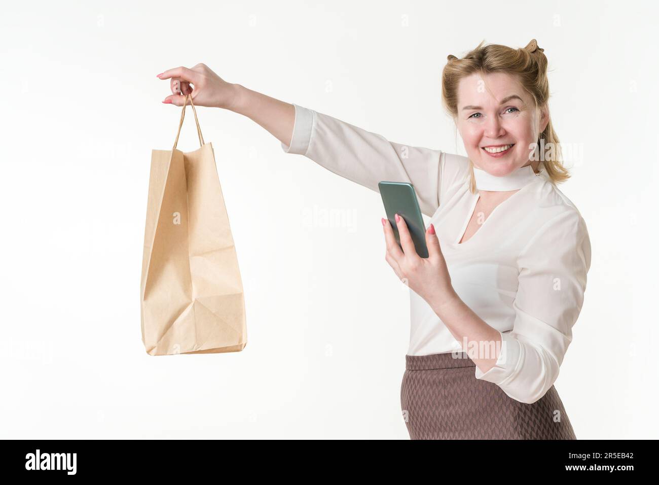 Fröhliche Käuferin, die Einwegpapiertaschen in ausgestreckter Hand hält und mit dem Smartphone bargeldlos bezahlt. Lächelnde Frau Stockfoto