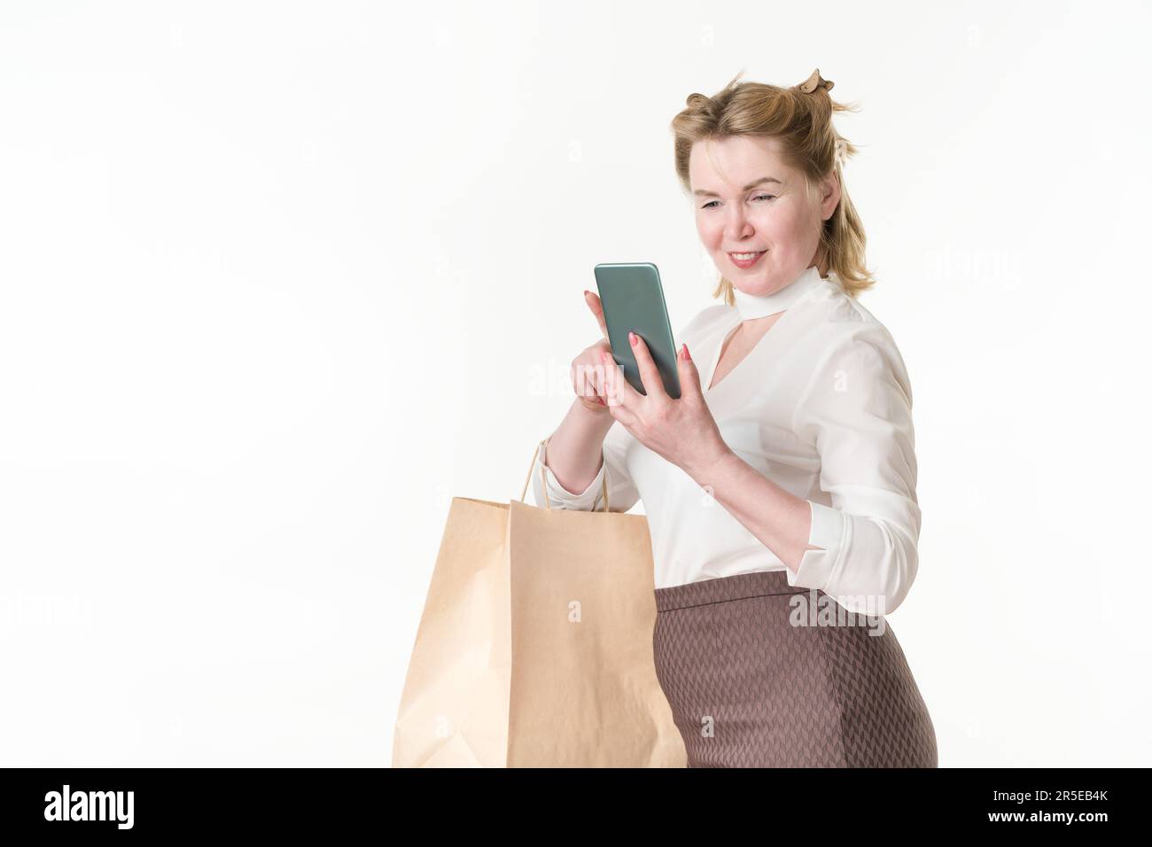 Fröhliche Frau beim Einkaufen, mit dem Smartphone auf den Bildschirm schauen, Online-Nachrichten lesen und Angebote mit Sonderangeboten und Rabatten durchstöbern Stockfoto