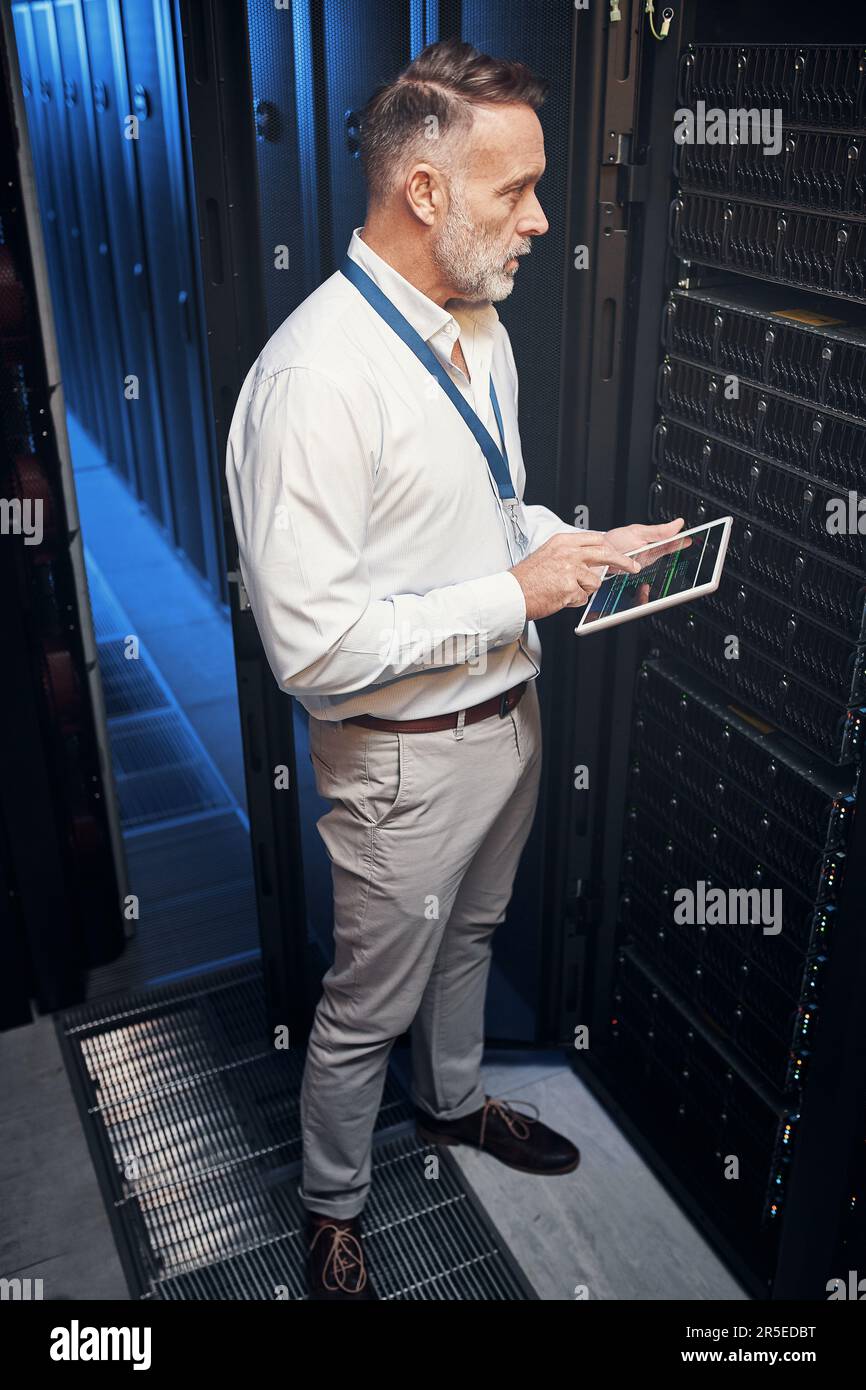 Ein Anruf und du bist verdammt noch mal verbunden. Ein erwachsener Mann, der ein digitales Tablet verwendet, während er in einem Serverraum arbeitet. Stockfoto