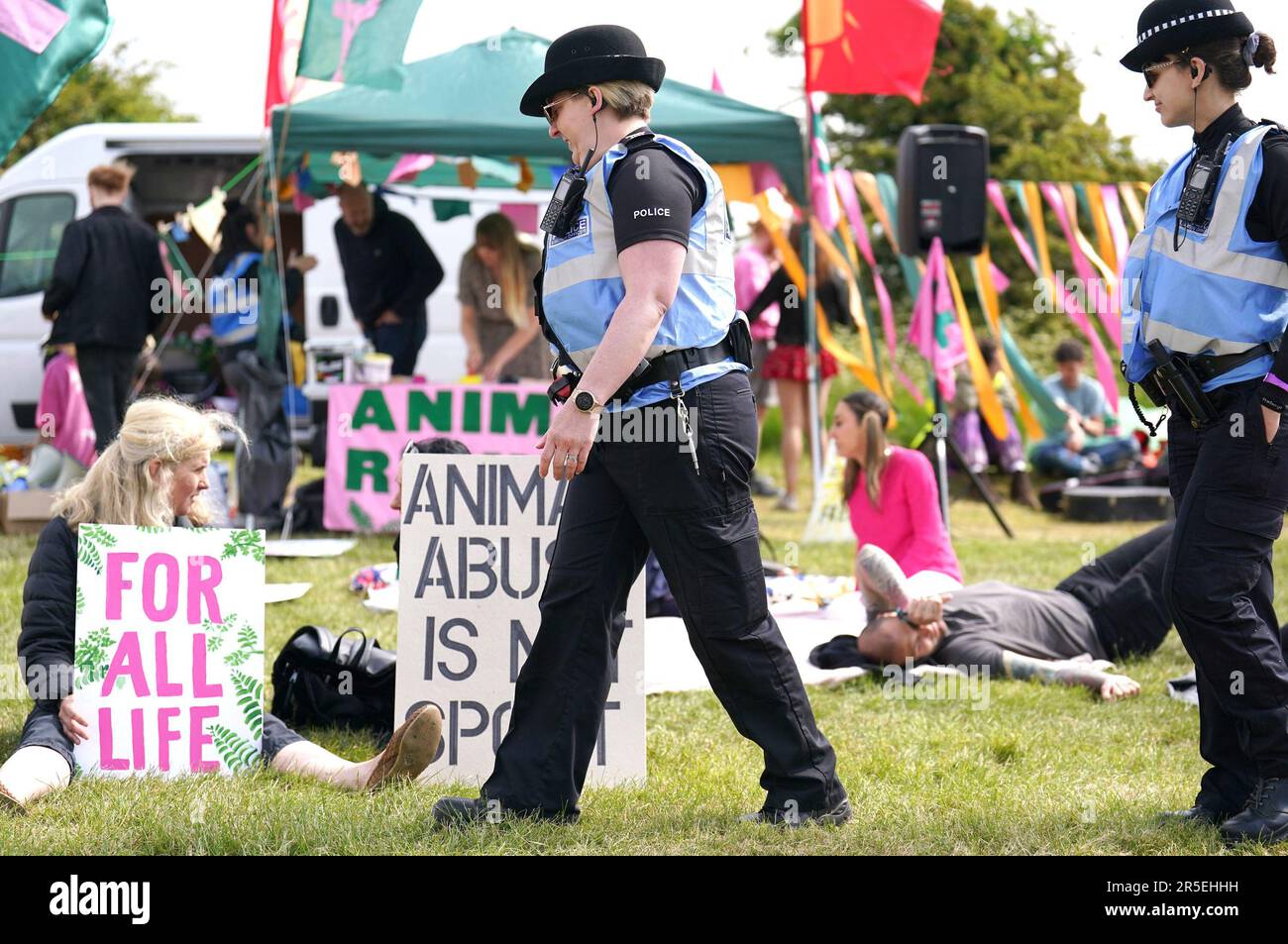 Polizeibeamte gehen vorbei an Mitgliedern der Tierschutzprotestgruppe Animal Rising, nachdem ihnen vom Jockey Club ein Platz zugewiesen wurde, in der Nähe des Rennbahneingangs, um während des Derby Festivals auf der Epsom Downs Rennbahn, Epsom, zu demonstrieren. Foto: Samstag, 3. Juni 2023. Stockfoto