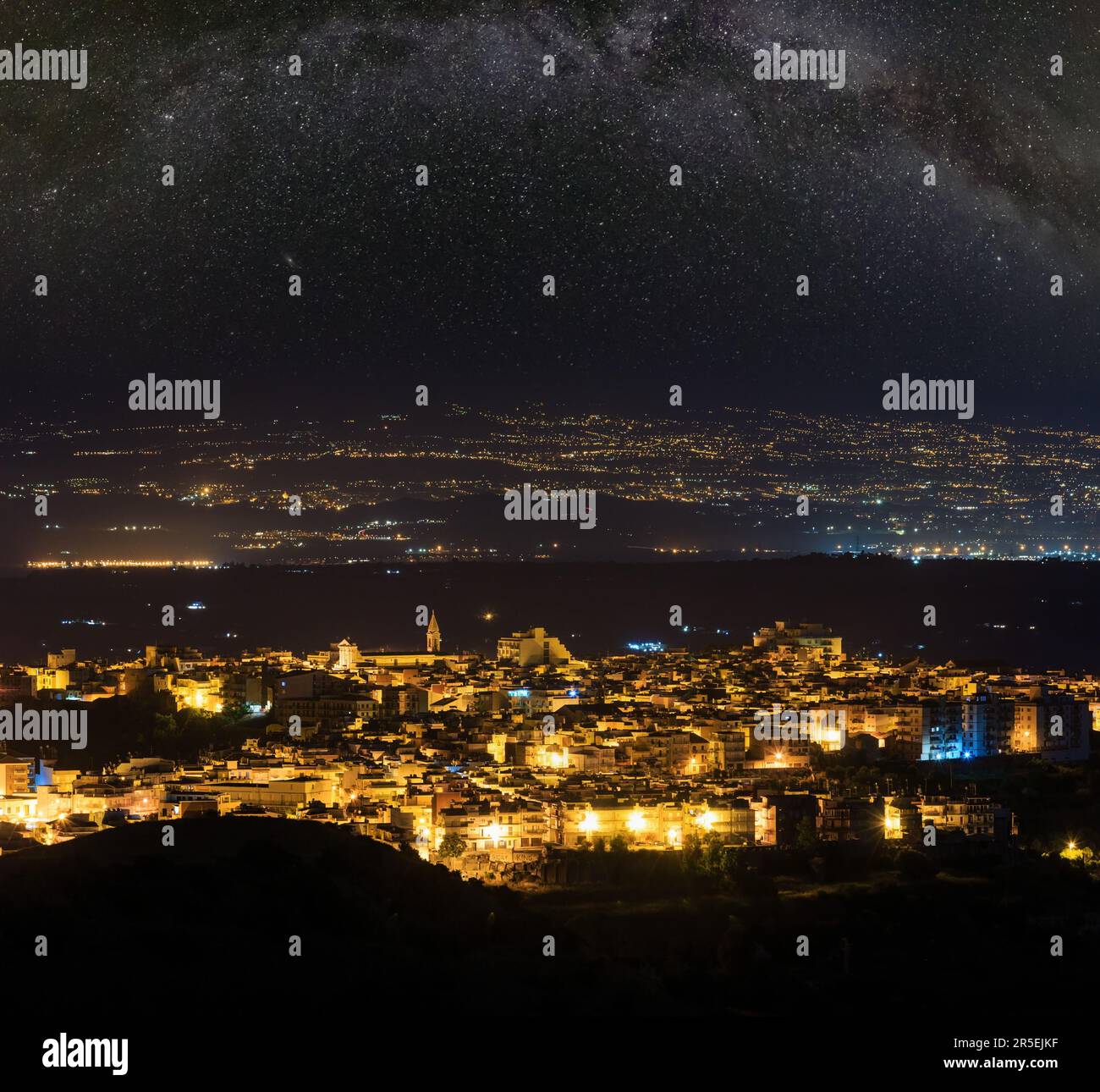Blick auf die Stadt Lentini bei Nacht in Richtung Bergstraße zum Meer und Ätna-Vulkan (Siracusa, Sizilien, Italien) und die Milchstraße oben. Stockfoto