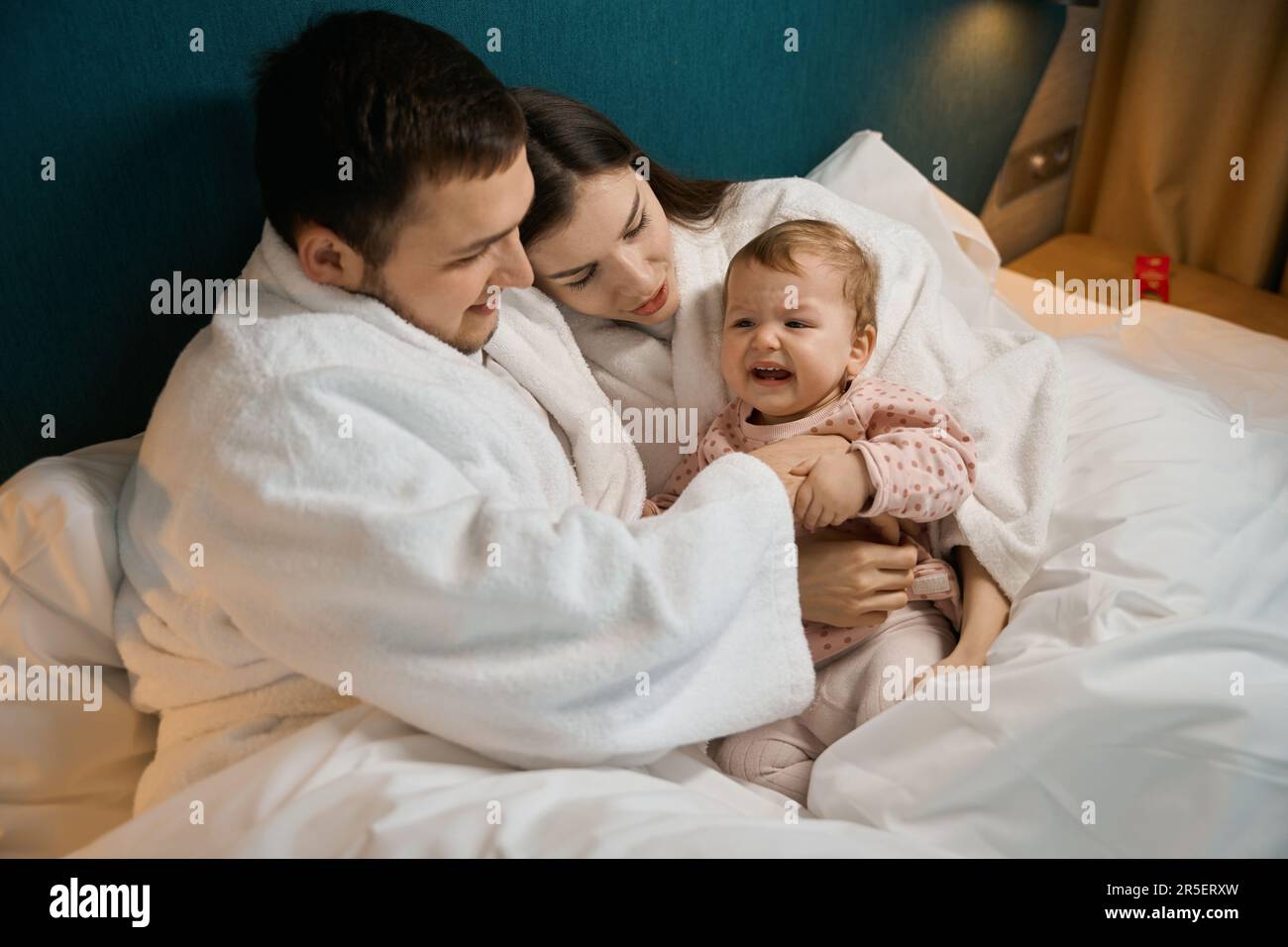 Ein kleines Kind ist unartig mit Eltern in einem großen Bett Stockfoto