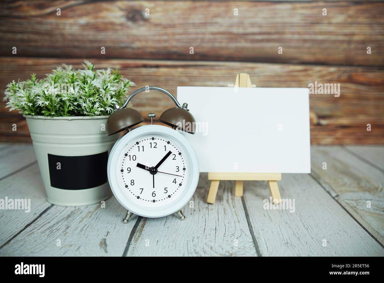 Leeres Kartenmodell mit künstlicher Pflanze und weißer Alarmklingel auf Holzhintergrund Stockfoto