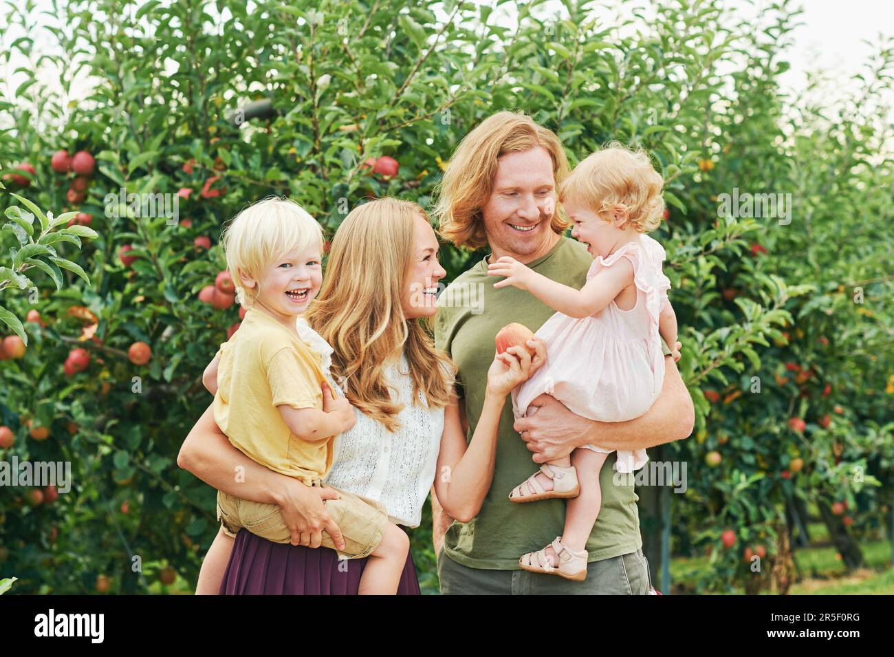 Außenporträt einer glücklichen jungen Familie mit zwei kleinen Kindern, die sich im Apfelgarten amüsieren Stockfoto