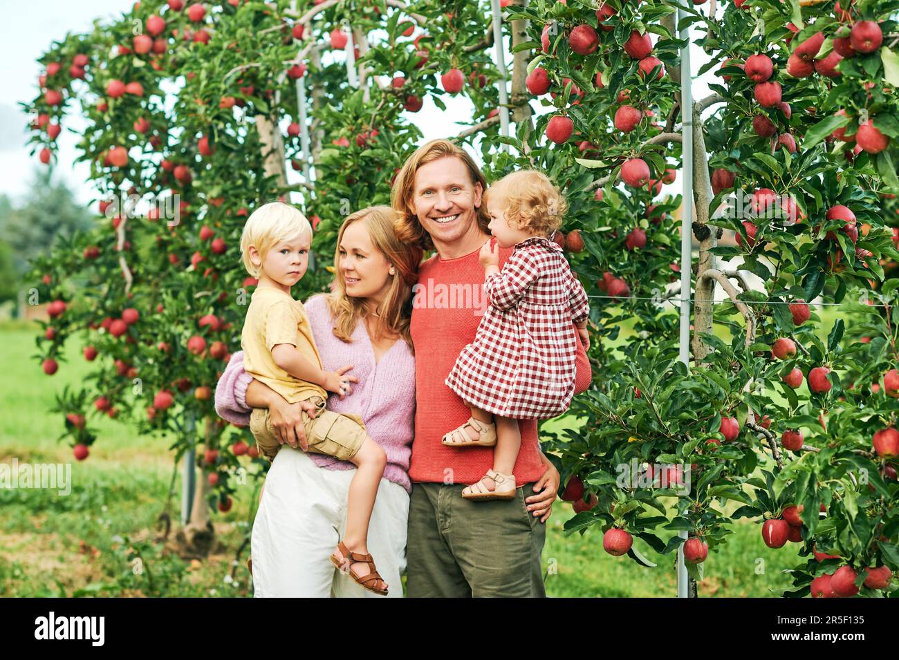 Außenporträt einer glücklichen jungen Familie mit zwei kleinen Kindern, die sich im Apfelgarten amüsieren Stockfoto