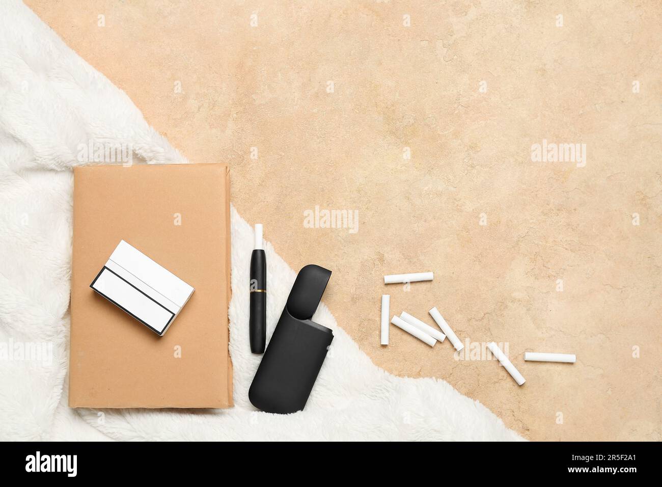 Komposition mit moderner elektronischer Zigarre, Stäbchen und Buch auf beigefarbenem Tisch Stockfoto