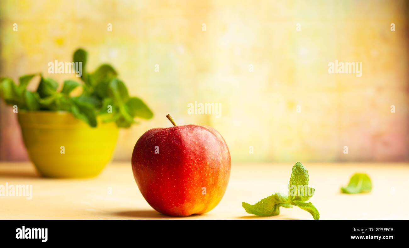 Stillleben mit rotem Apfel und frischer Minze in der Schüssel auf gelbem Hintergrund. Vorderansicht, Kopierbereich. Stockfoto