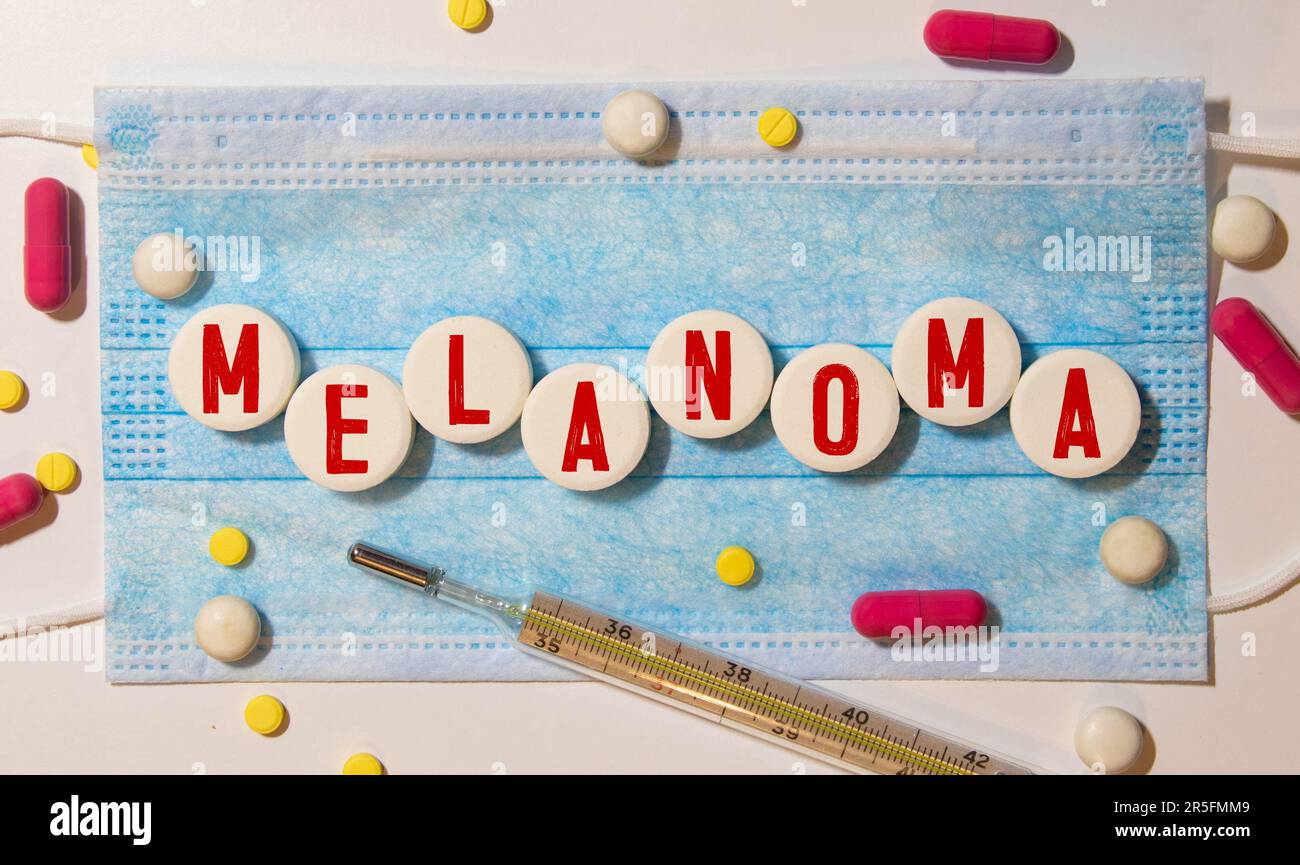 Das Wort MELANOM steht auf Holzblöcken auf blauem Hintergrund in der Nähe der Pillen. Medizinisches Konzept. Stockfoto