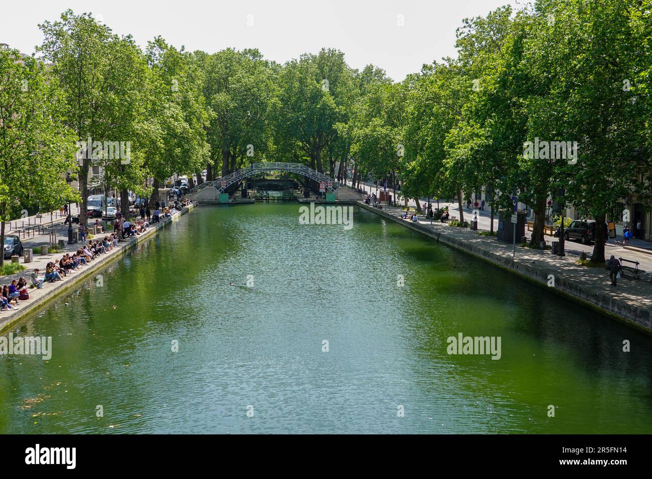 Junge Leute säumen die Ufer des Canal Saint-Martin und entspannen in der warmen Sonne an einem Freitagnachmittag, 10. Arrondissement, Paris, Frankreich. Stockfoto