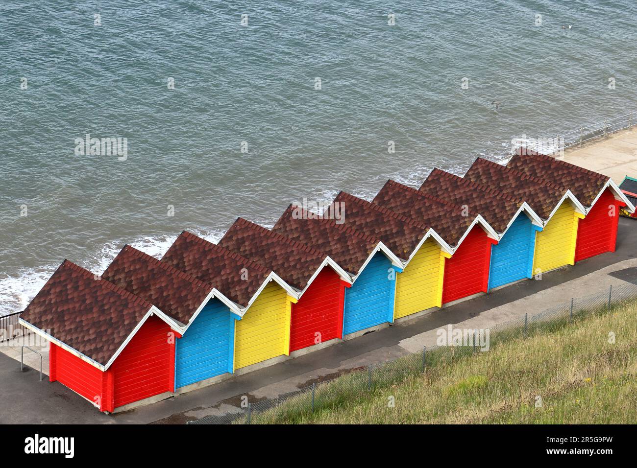 Eine Reihe farbenfroher Strandhütten entlang der Promenade von Whitby, von oben und hinten mit dem Meer im Hintergrund Stockfoto