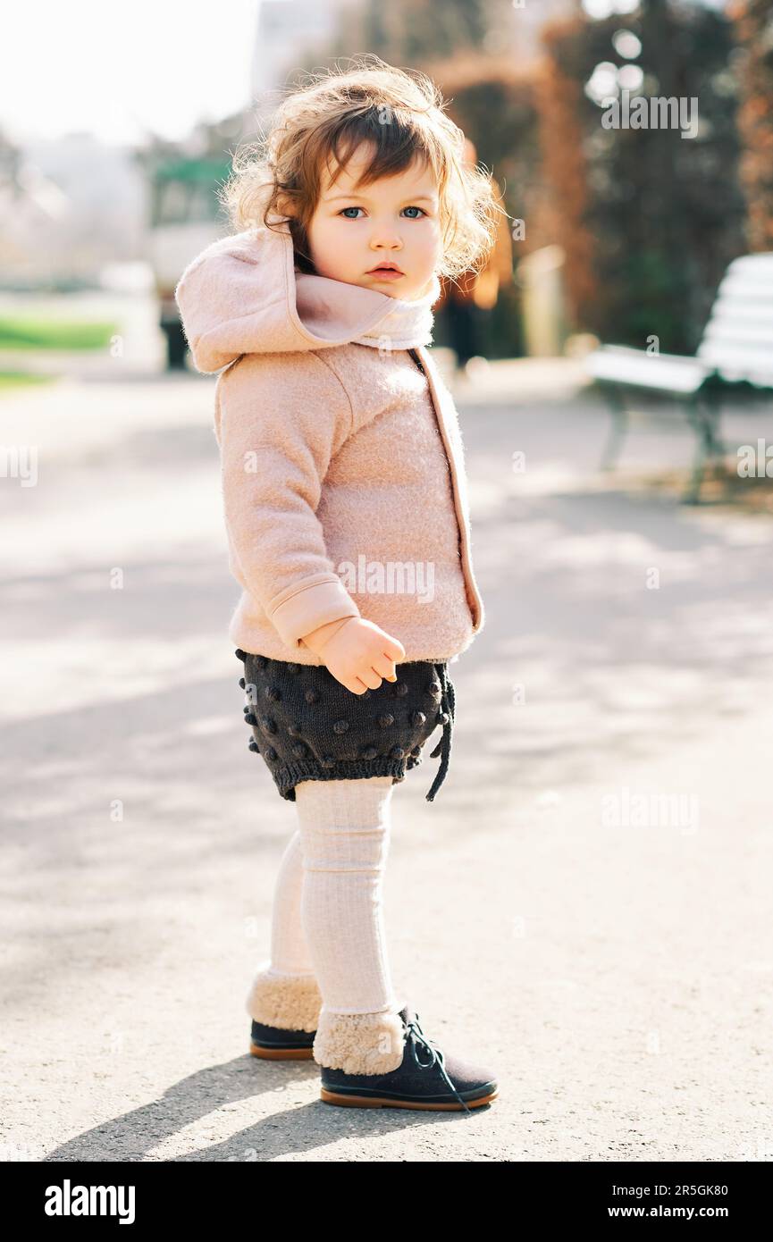 Außenporträt eines niedlichen Kleinkindes mit lockigem Haar, in einer warmen rosa Jacke und bei kaltem Wetter Stockfoto