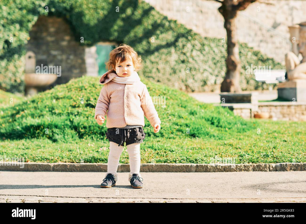Außenporträt eines bezaubernden 1 - 2 Jahre alten Kleinkindes, das eine warme rosa Jacke trägt und im Park spielt Stockfoto
