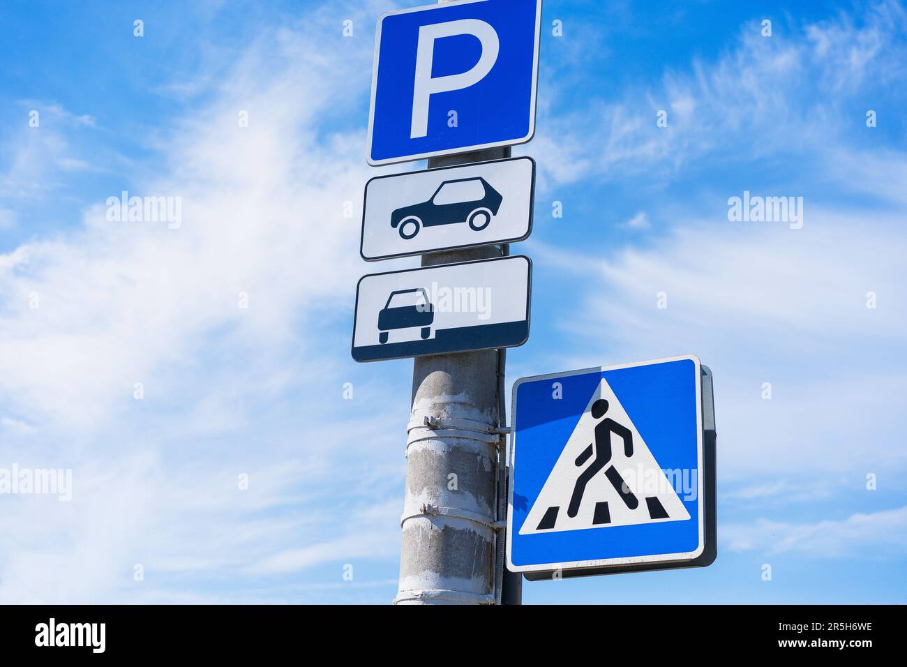 Parkschild für Personenkraftwagen mit Hinweis auf einen Parkplatz am Straßenrand mit einer Überquerung auf einem Betonpfahl vor blauem Himmelshintergrund Stockfoto