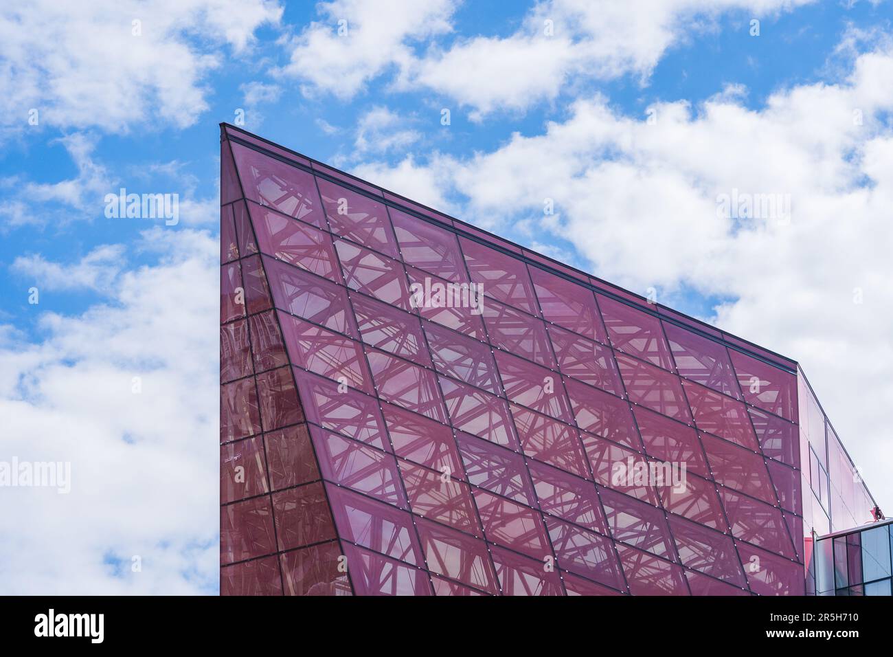 Stilvolle Glasfassade aus Violett getöntem, halbtransparentem Glasgebäude mit Sonnenstrahlen am blauen Himmel. Modernes Architekturkonzept Stockfoto