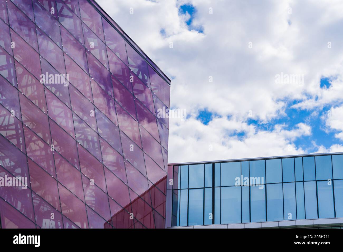 Stilvolle Glasfassade aus Violett getöntem, halbtransparentem Glasgebäude mit Sonnenstrahlen am blauen Himmel. Modernes Architekturkonzept Stockfoto