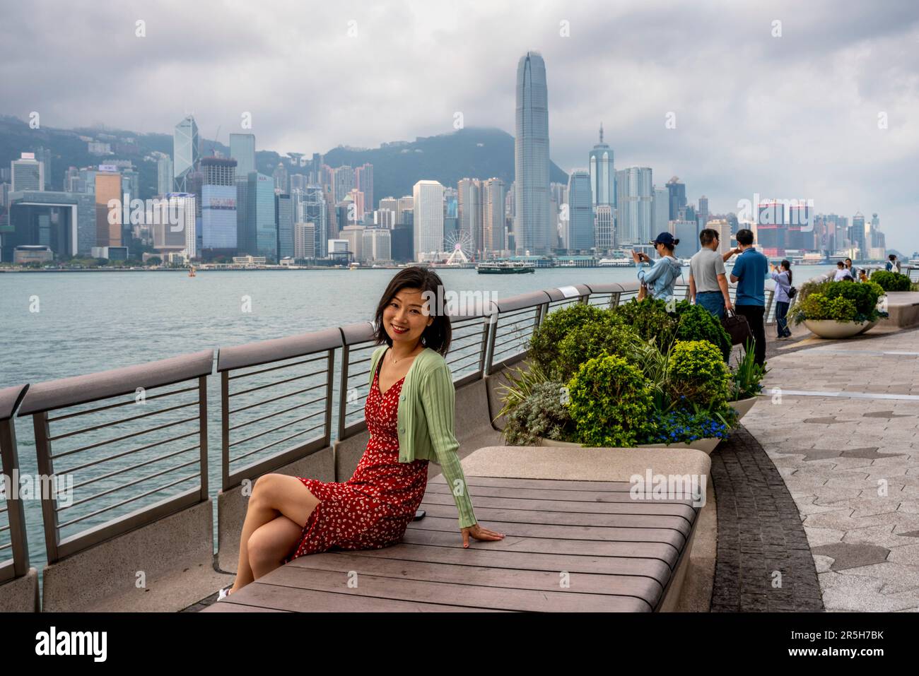 Eine attraktive junge Chinesin posiert für Ein Foto auf der Avenue of Stars mit Hong Kong Island als Kulisse, Kowloon, Hongkong, China. Stockfoto