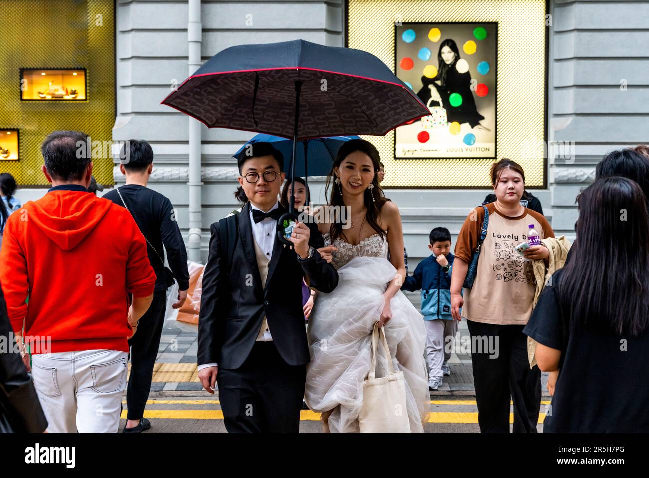 Ein frisch verheiratetes Paar, das Eine Straße überquert in Kowloon, Hongkong, China. Stockfoto