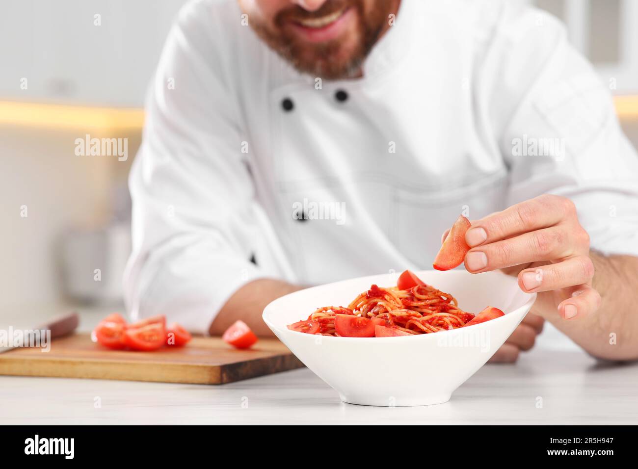 Nahaufnahme des professionellen Küchenchefs, der Tomaten in die Schüssel mit köstlichen Spaghetti am Marmortisch in der Küche gab, konzentriert sich auf Essen Stockfoto