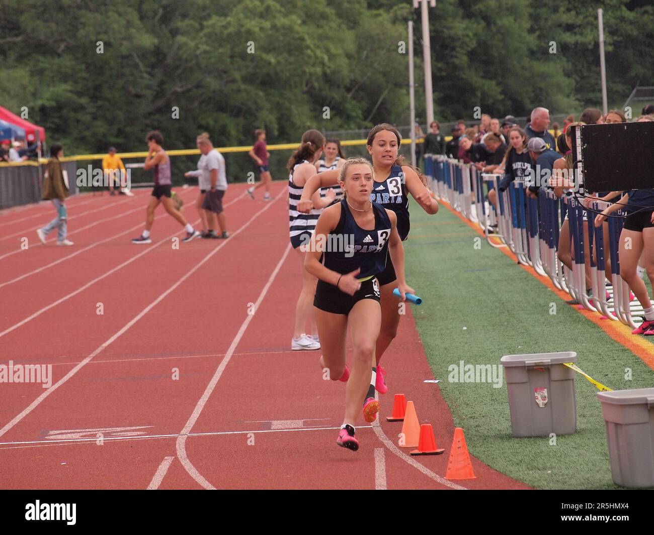 Highschool-Sprinter kämpfen um ein 400 Meter langes Staffelrennen. Entschlossenheit und Stärke werden auf den Flächen der Mitbewerber angegeben. Stockfoto