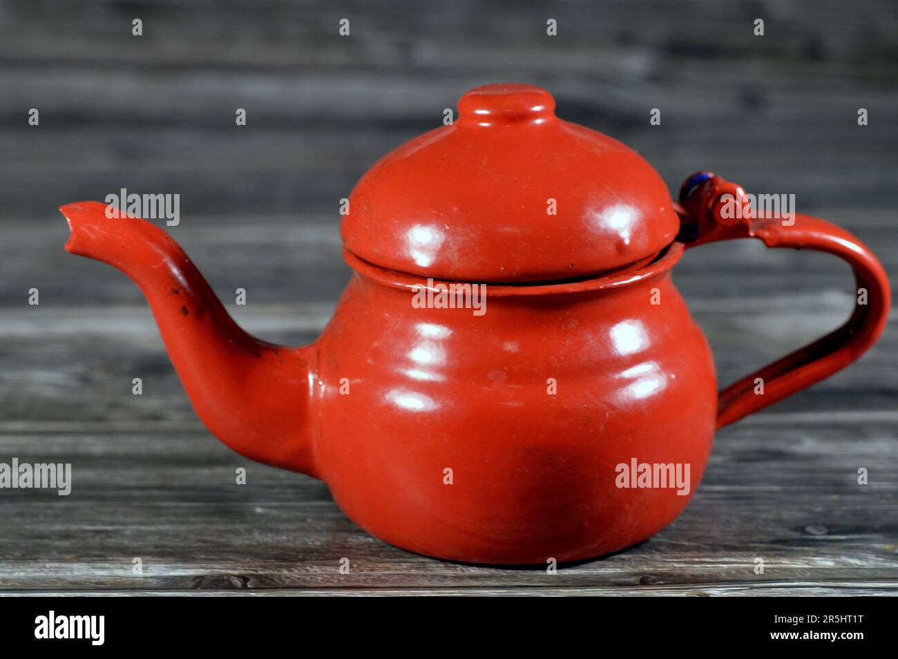 Eine altmodische Teekanne im Retro-Stil, eine rote Teekanne auf Holzhintergrund, ein Behälter zum Zubereiten und Servieren von Tee mit einem Griff und einer geformten Öffnung Stockfoto