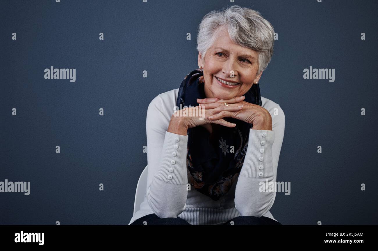 Ich bin heutzutage eine glückliche Frau. Studioaufnahme einer fröhlichen älteren Frau, die mit den Händen unter dem Kinn in der Ferne sitzt. Stockfoto