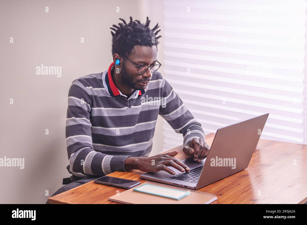 Ein junger afrikanischer Mann, der fleißig an seinem Laptop an einem sauberen und gut beleuchteten Schreibtisch arbeitet – eine konzentrierte und produktive Arbeitsumgebung Stockfoto