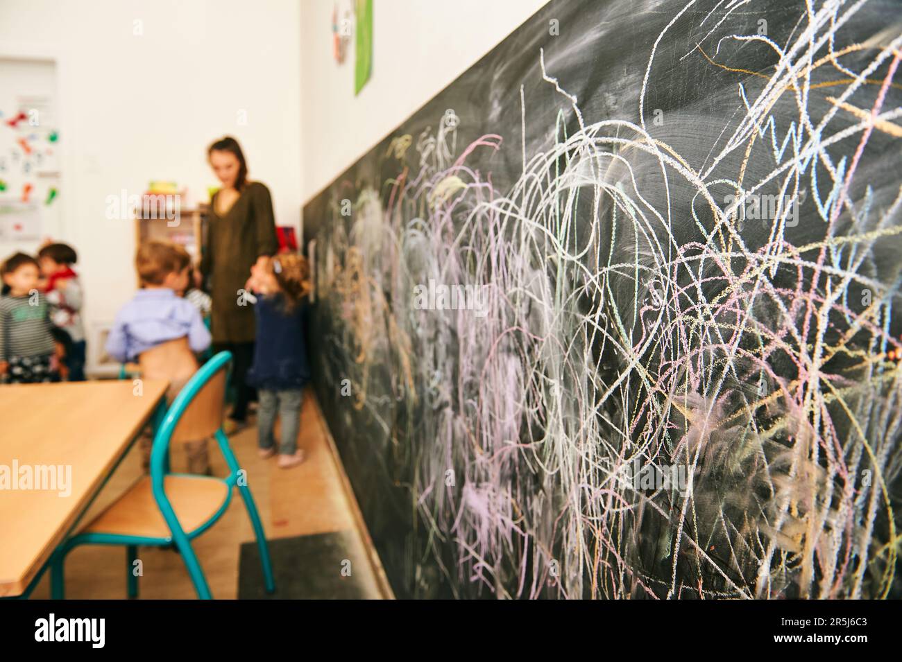 Kunstunterricht im Kindergarten, junger Lehrer malt mit Kindern an der Kreidewand Stockfoto