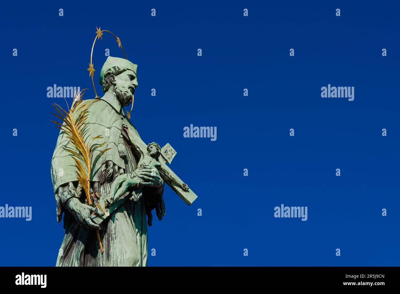 Heiliger Johannes von Nepomuk, Schutzpatron und Märtyrer von Böhmen. Bronzestatue mit Kruzifix, errichtet auf der Prager Karlsbrücke im Jahr 1683 (mit blauem Himmel und Kopierspieß Stockfoto