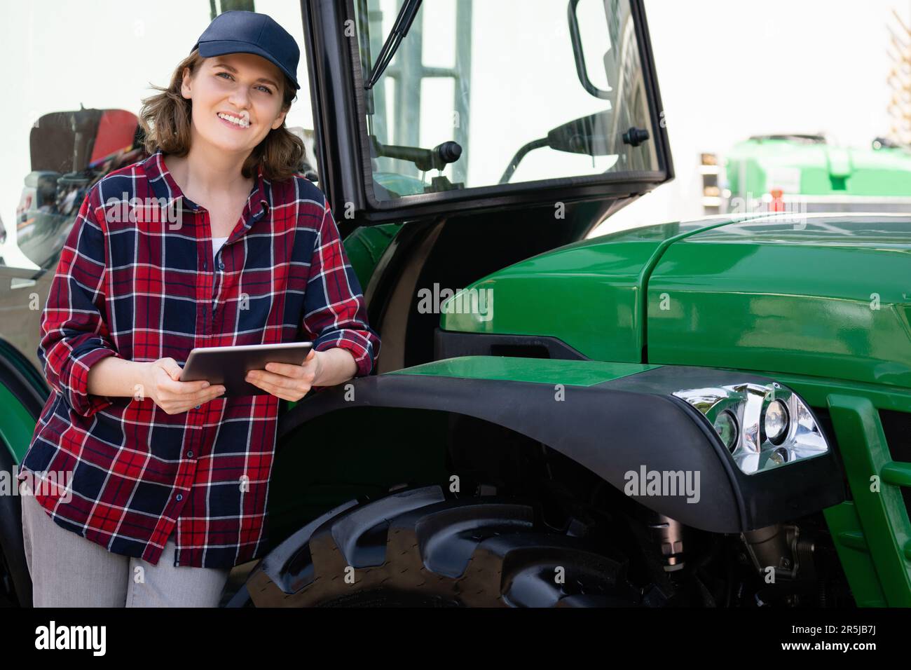 Landwirtin mit einem digitalen Tablet auf dem Hintergrund eines landwirtschaftlichen Traktors Stockfoto