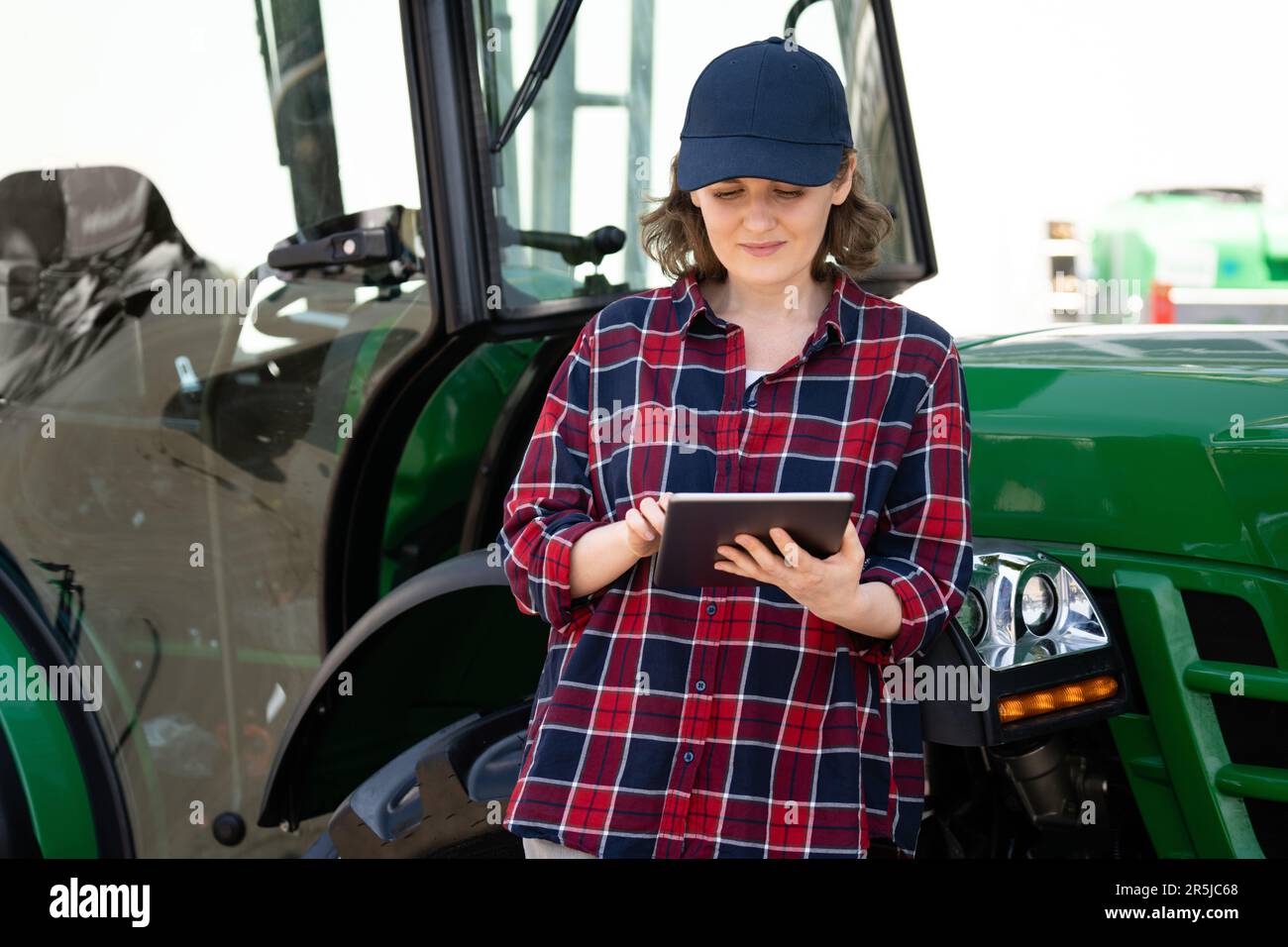 Landwirtin mit einem digitalen Tablet auf dem Hintergrund eines landwirtschaftlichen Traktors Stockfoto