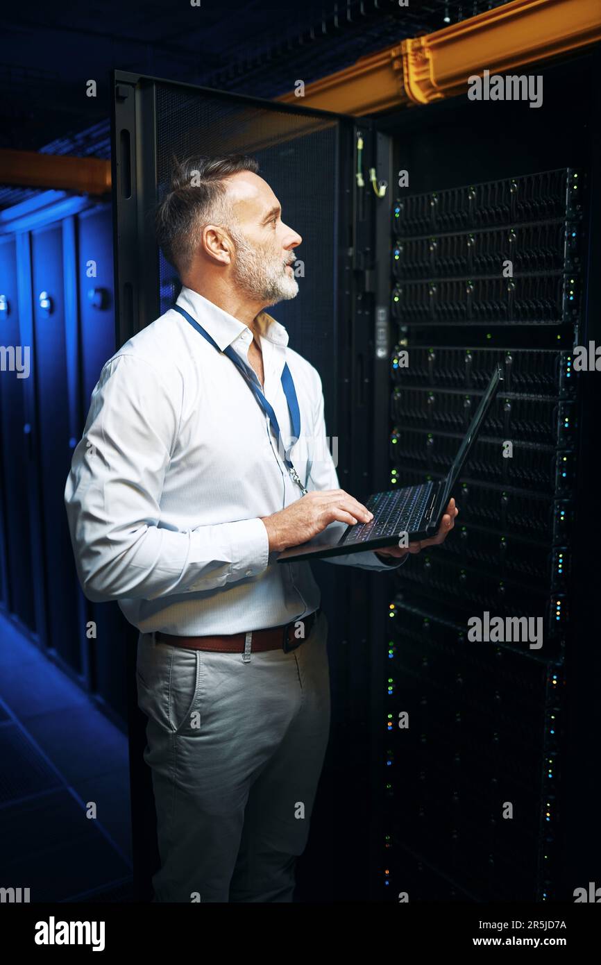 Es gibt eine bestimmte Art, alles miteinander zu verbinden. Ein erwachsener Mann, der ein Notebook verwendet, während er in einem Serverraum arbeitet. Stockfoto
