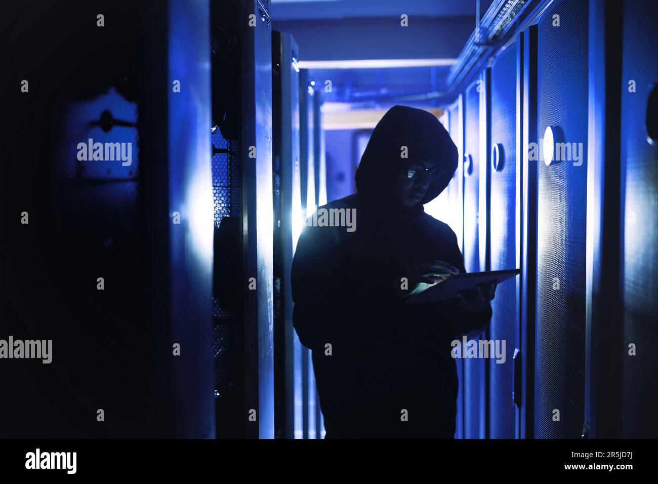 Cyberkriminalität kann uns alle betreffen. Ein Hacker, der ein digitales Tablet in einem Serverraum verwendet. Stockfoto