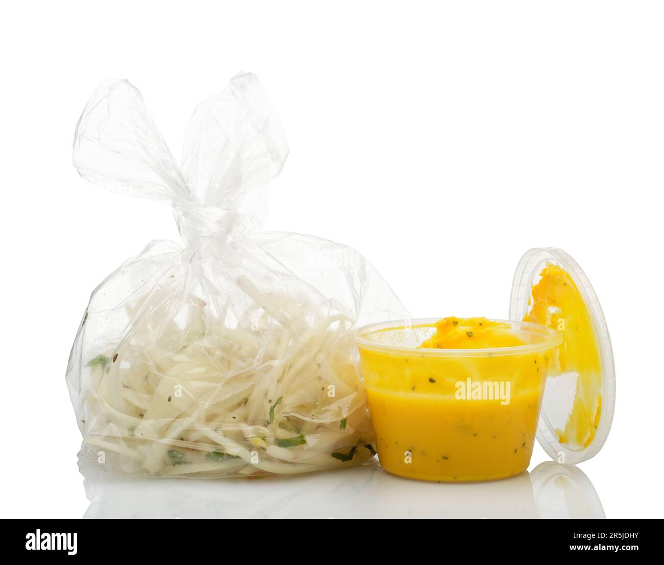 Bei einem indischen Essen zum Mitnehmen wurden Sachen hinzugefügt (aber nicht immer gegessen). Gehackte Zwiebeln in einer Plastiktüte und gelbe Dippsoße. Stockfoto