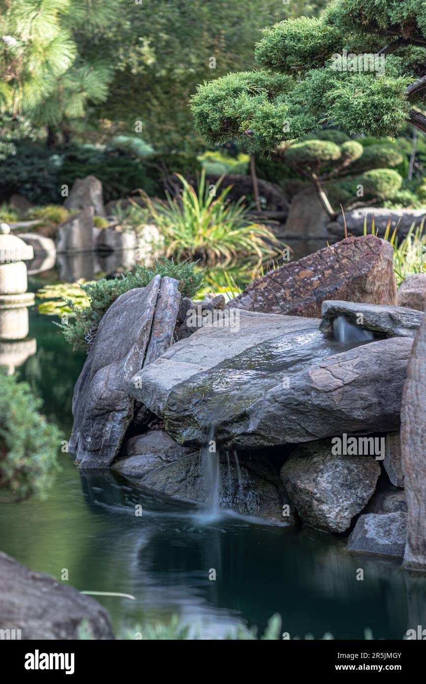 Üppiger japanischer Garten mit einem ruhigen Fluss und großen Felsen Stockfoto