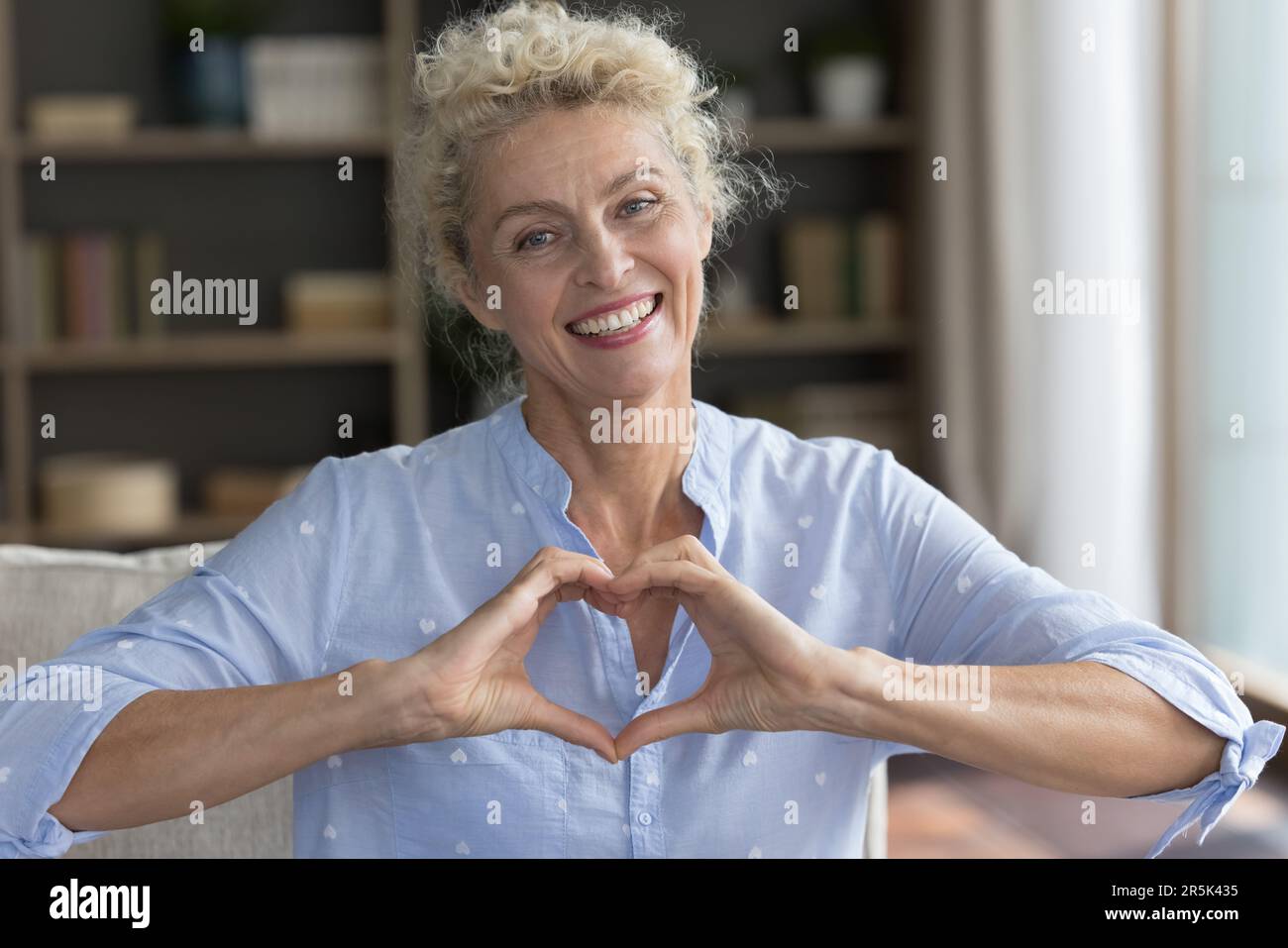 Fröhliche, positive, ziemlich reife Frau, die Fingerherz auf die Brust legt Stockfoto
