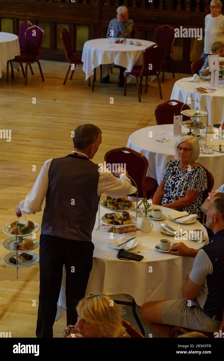 Ein männlicher Kellner serviert den Gästen im Royal Hall, Harrogate, North Yorkshire, England, Großbritannien, auf zwei dreistöckigen Tabletts köstliche Speisen und Kuchen. Stockfoto