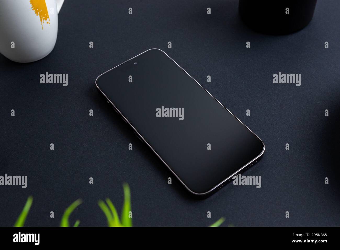 Leeres Telefon auf schwarzem Tisch. Pflanzen, Kaffeebecher und Kugelschreiber nebenan. Professionelles Geschäftsgebaren Stockfoto