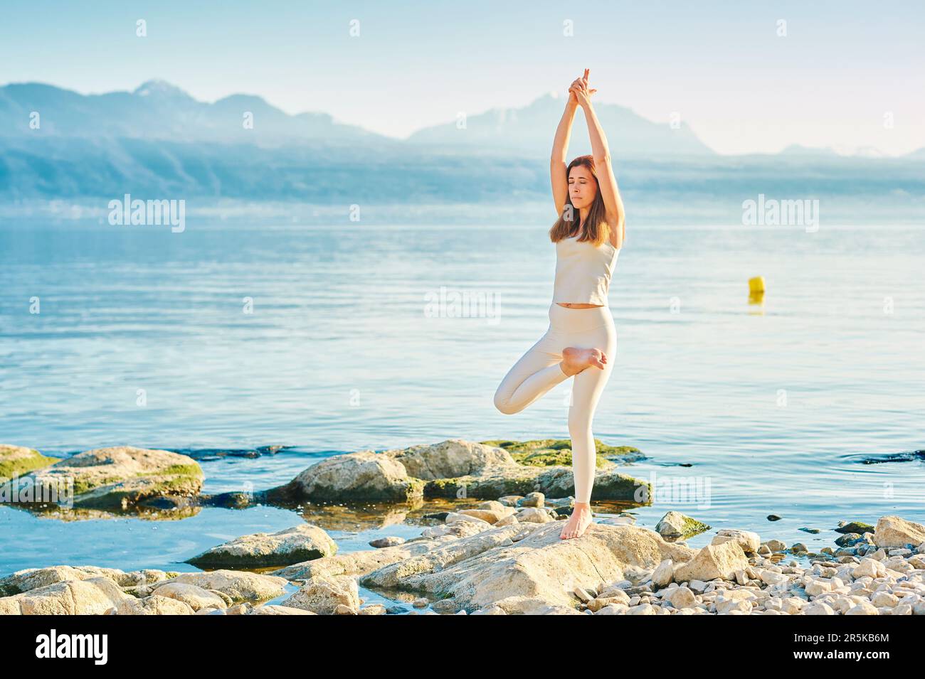 Wunderschöne gesunde Frau, die Yoga-Übungen draußen am wunderschönen Bergsee praktiziert Stockfoto