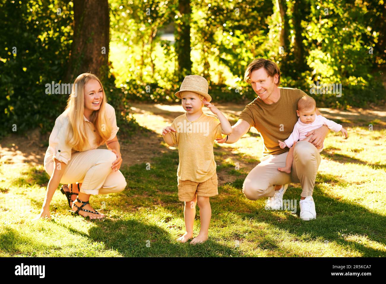 Außenporträt einer glücklichen Familie, die Spaß im Sommerpark hat, ein junges Paar mit einem kleinen Jungen und einem kleinen Mädchen Stockfoto