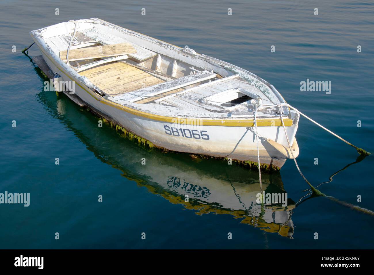 Sibenik, Kroatien - 31. Mai 2023: Ein altes, weiß verwittertes Ruderboot, das in ruhigem Meerwasser gefesselt ist und sich reflektiert Stockfoto