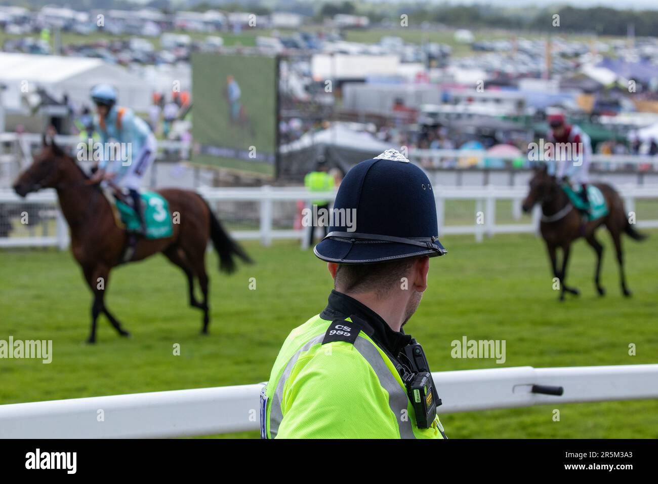 Epsom, Großbritannien. 3. Juni 2023. Rennpferde und Jockeys fahren am Tag des Epsom Derby hinter einem Polizisten von Sussex entlang der Rennbahn Epsom Downs. £150.000 wurden für zusätzliche Sicherheitsmaßnahmen ausgegeben, um einem geplanten Protest von Aktivisten von Animal Rising entgegenzuwirken, die Pferderennen als grausame und ausbeuterische Industrie ansehen. Die Polizei von Surrey berichtete, dass 31 Verhaftungen vorgenommen wurden, einschließlich 19 präventiven Verhaftungen. Kredit: Mark Kerrison/Alamy Live News Stockfoto