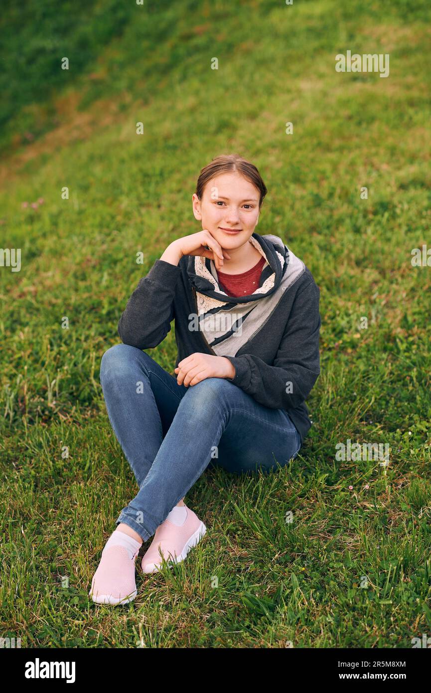 Außenporträt eines süßen jungen Mädchens, das auf einem grünen, frischen Rasen sitzt Stockfoto