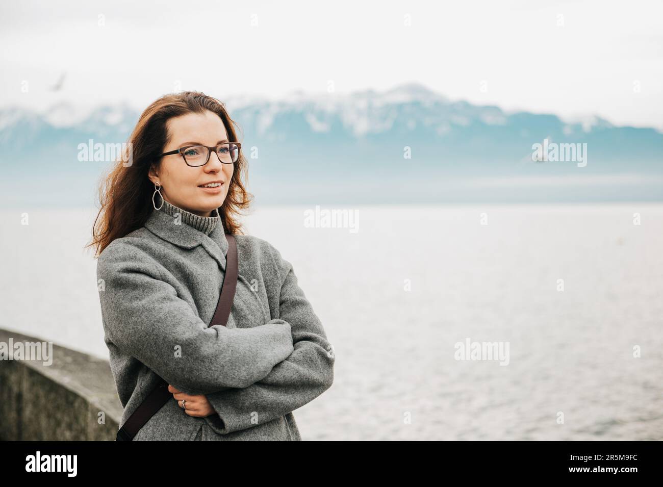 Außenporträt einer schönen Frau, trägt einen grauen Mantel, posiert neben dem See Stockfoto