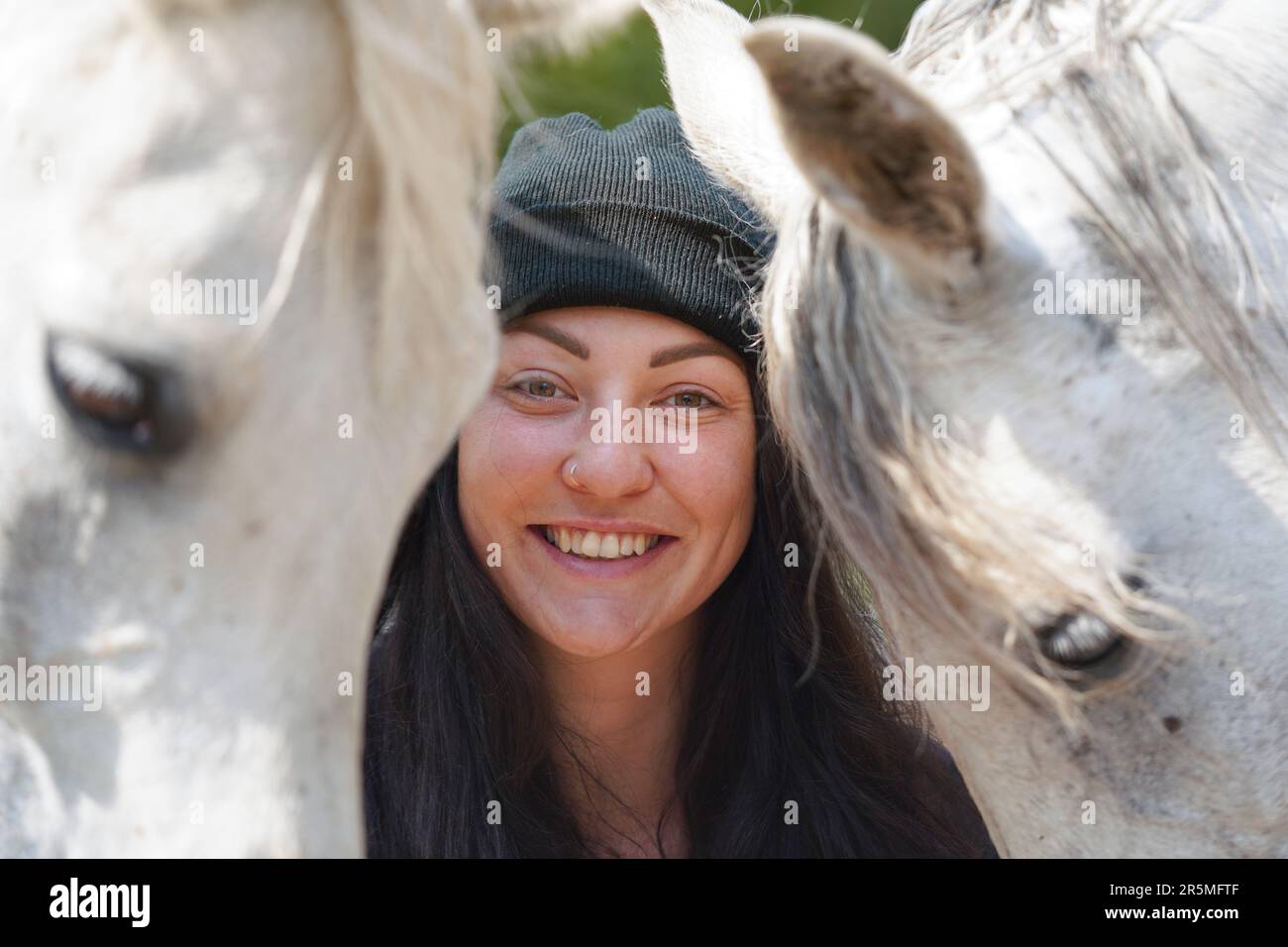 Junge Frau, die hinter zwei weißen arabischen Pferden steht und glücklich lächelt, einer auf jeder Seite, Nahaufnahme Stockfoto