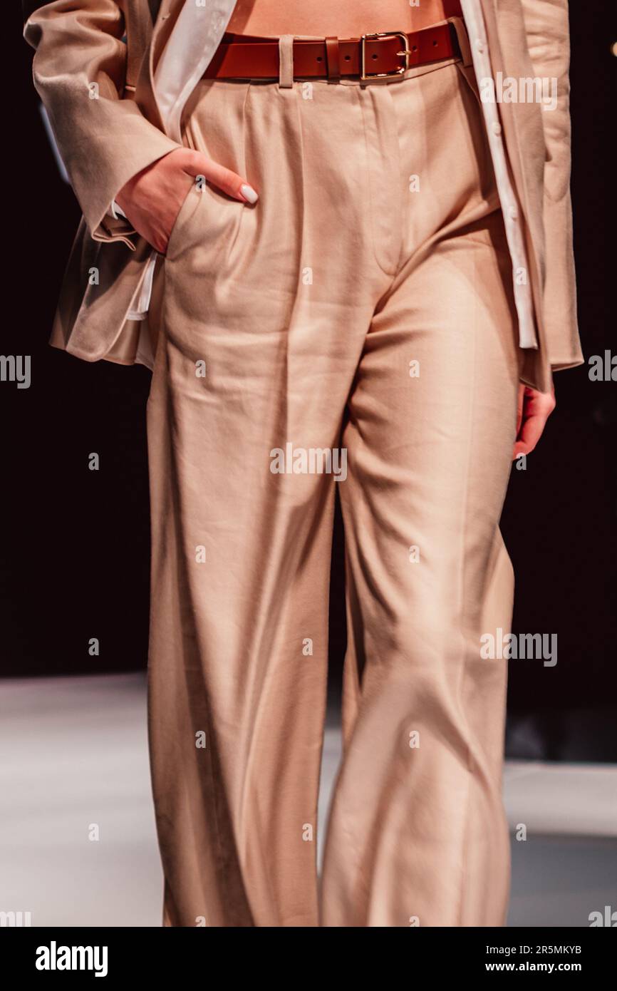 Schicke Details in stilvollem, neutralbeigem Outfit, stilvolle Jacke, Hose mit braunem Ledergürtel. Textilkonzept Unisex. Vertikal Stockfoto