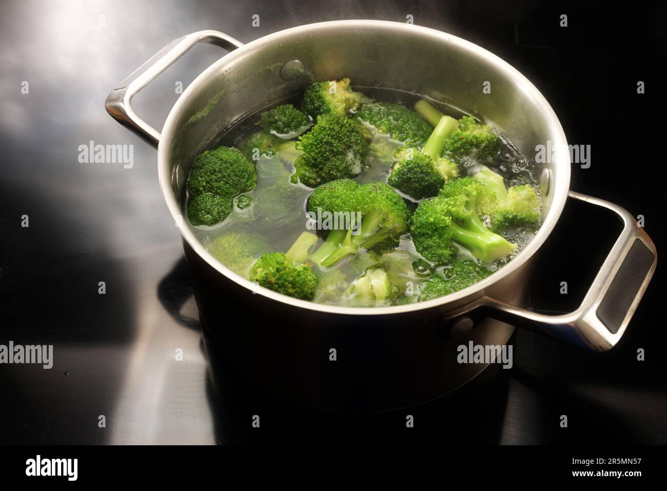 Kochen von Brokkoli in kochendem Wasser in einem Edelstahltopf auf dem schwarzen Kochfeld in der Küche, Vorbereitung auf eine gesunde Gemüsesaal, Kopierraum, Stockfoto