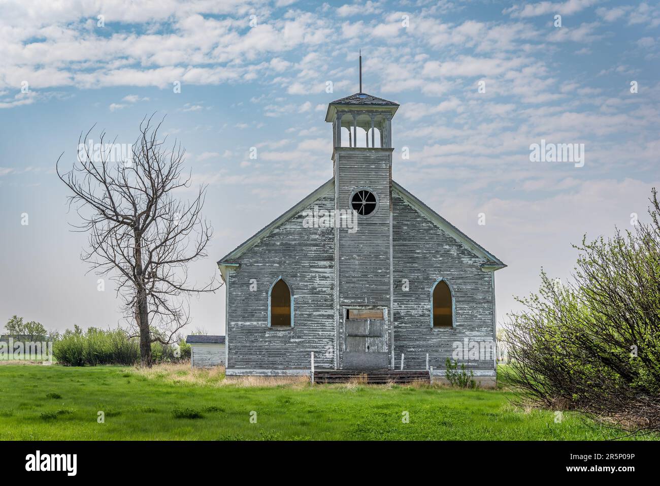 Die verlassene römisch-katholische Kirche Sainte-Jeanne d'Arc in Dollard, Saskatchewan, Kanada, mit Eulen in einem nahe gelegenen Baum Stockfoto