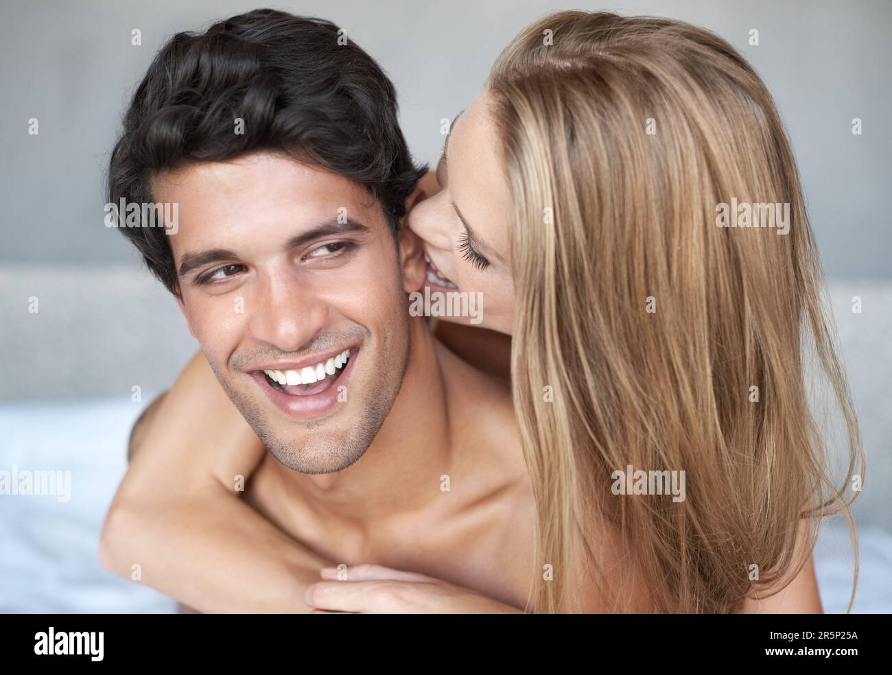 Grrrr ... Eine junge Frau umarmt ihren Freund von hinten, während sie sich verspielt ins Ohr beißt. Stockfoto