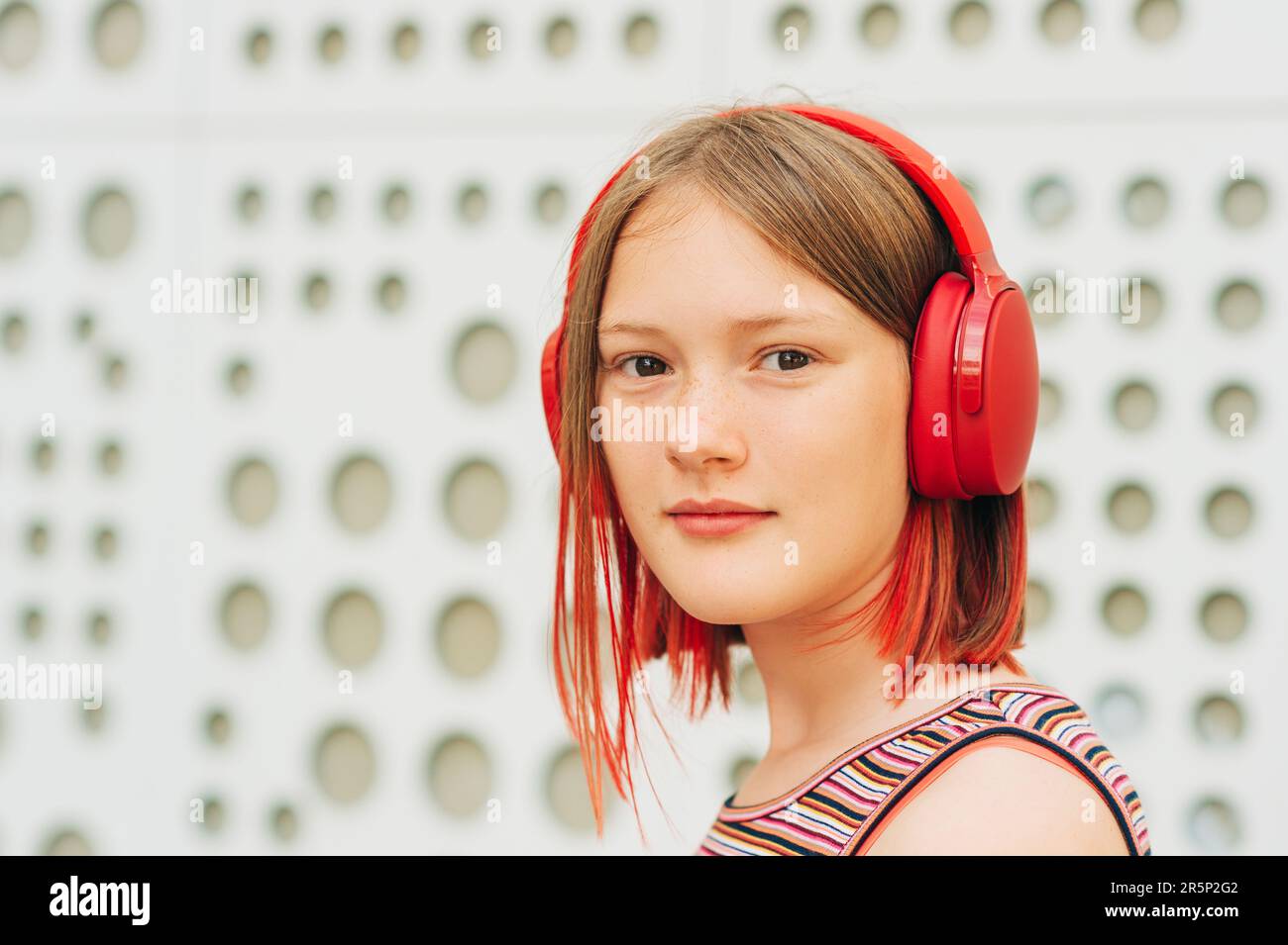 Außenporträt eines glücklichen jungen Mädchens mit stilvollem, rot gefärbtem kurzen Haar, das mit Kopfhörern Musik hört Stockfoto